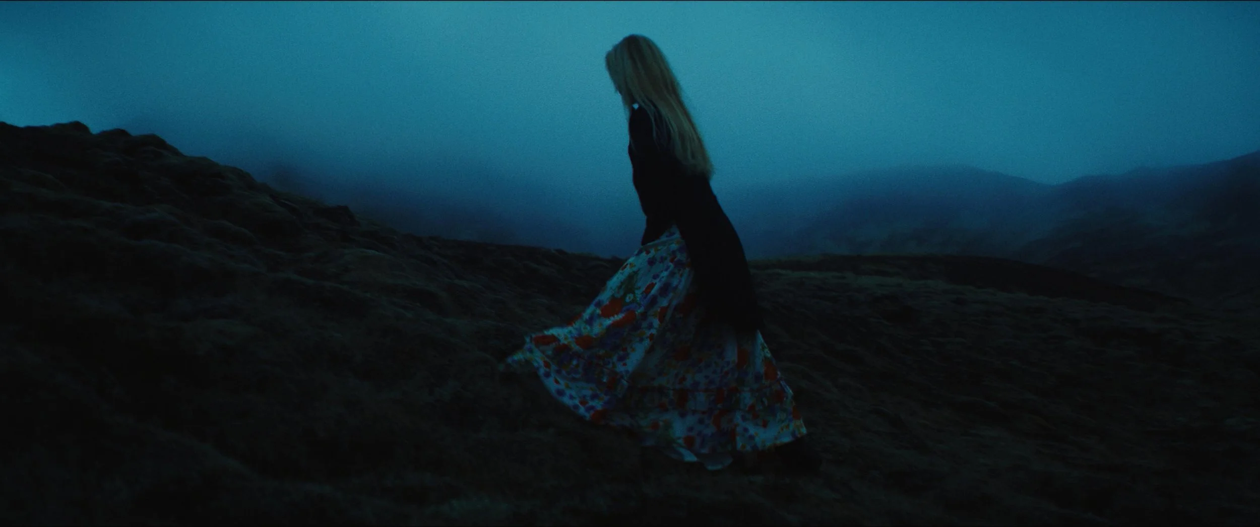 A lone figure crossing a misty moor at blue-hour dusk — a cinematic landscape still from Karma Film's Tina Dickow &lsquo;Fastland&rsquo; music video.